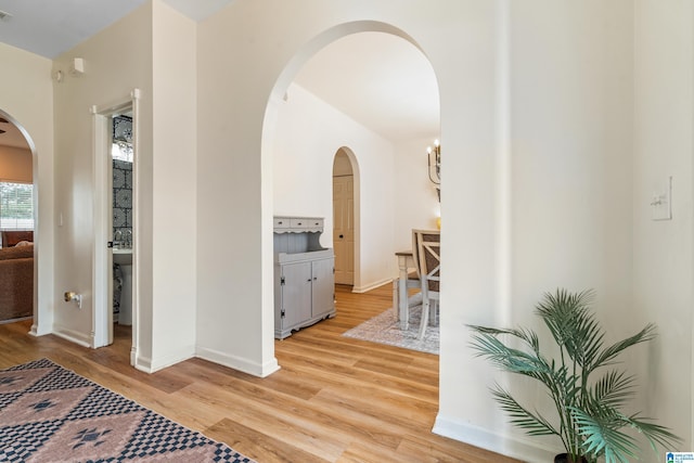 hallway with baseboards, arched walkways, light wood-style flooring, and visible vents
