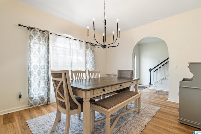 dining space with light wood-style floors, arched walkways, a chandelier, and stairway