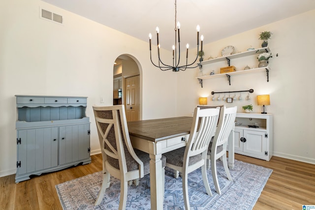 dining area featuring arched walkways, a notable chandelier, light wood-style flooring, and visible vents