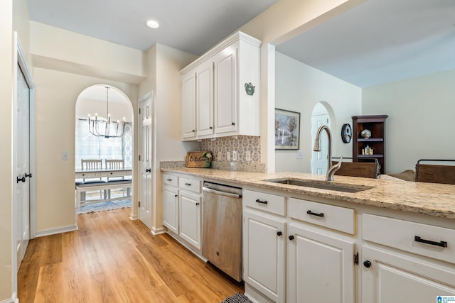 kitchen with arched walkways, dishwasher, a sink, light wood finished floors, and a chandelier