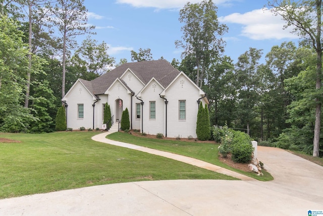french provincial home featuring roof with shingles, driveway, and a front yard