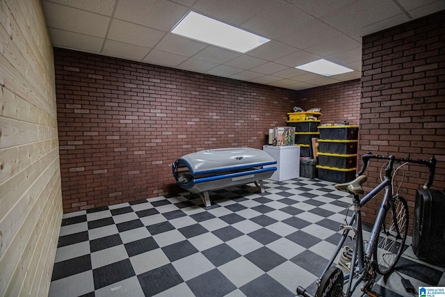 interior space with a paneled ceiling, tile patterned floors, and brick wall