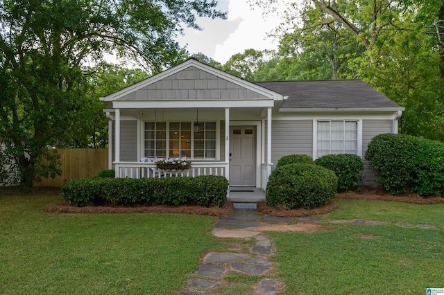 view of front of home with fence, roof with shingles, a porch, and a front lawn