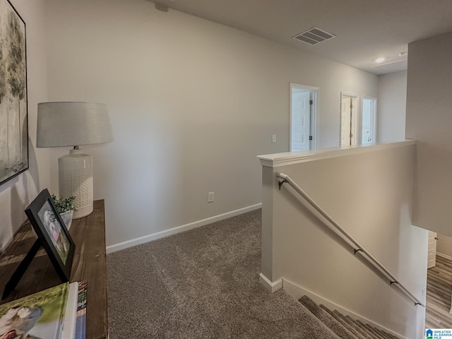 hallway featuring baseboards, carpet, visible vents, and an upstairs landing