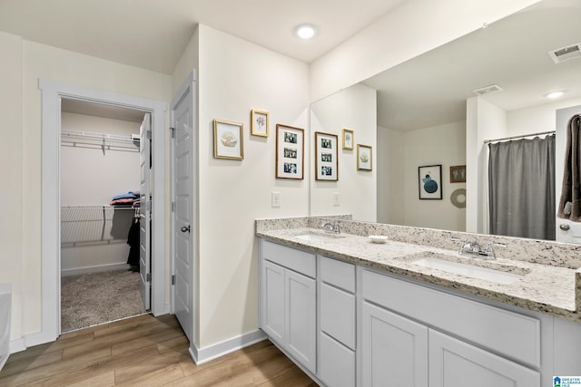 full bathroom featuring double vanity, visible vents, a sink, and wood finished floors
