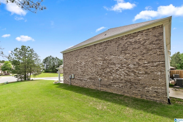 view of side of home featuring cooling unit, a yard, and brick siding