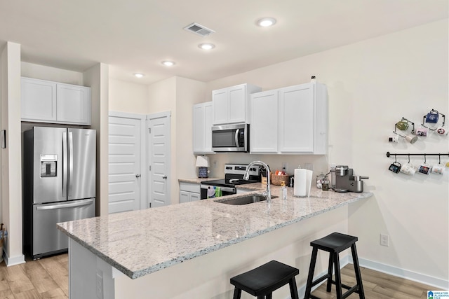 kitchen with appliances with stainless steel finishes, light stone counters, a sink, a breakfast bar area, and a peninsula
