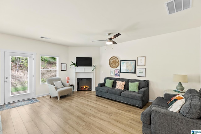 living room featuring visible vents, light wood-style floors, ceiling fan, and a warm lit fireplace