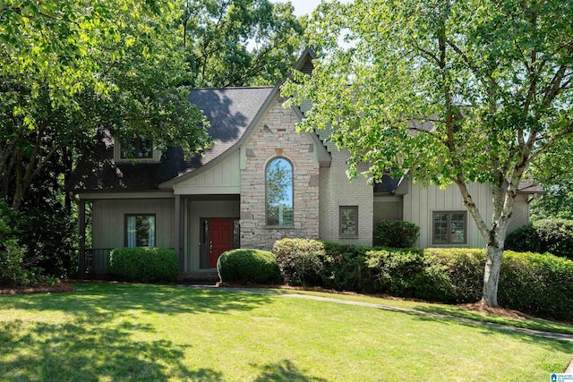 view of front of home featuring a shingled roof, a front yard, and stone siding