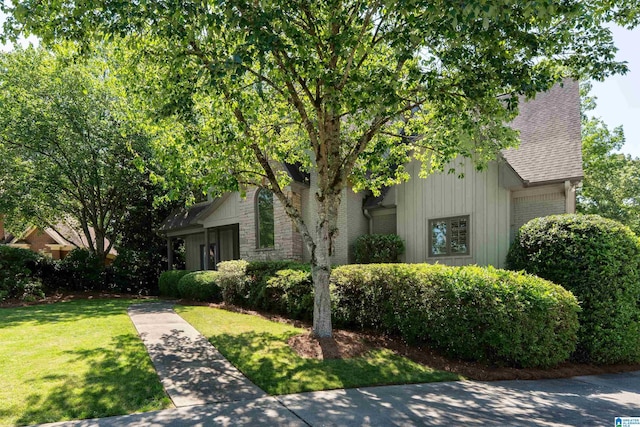 obstructed view of property featuring a garage, a front yard, brick siding, a shingled roof, and board and batten siding
