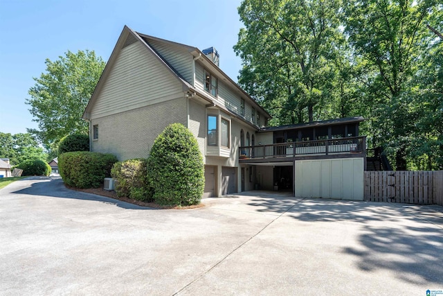 view of side of home with fence, an attached garage, brick siding, a chimney, and concrete driveway