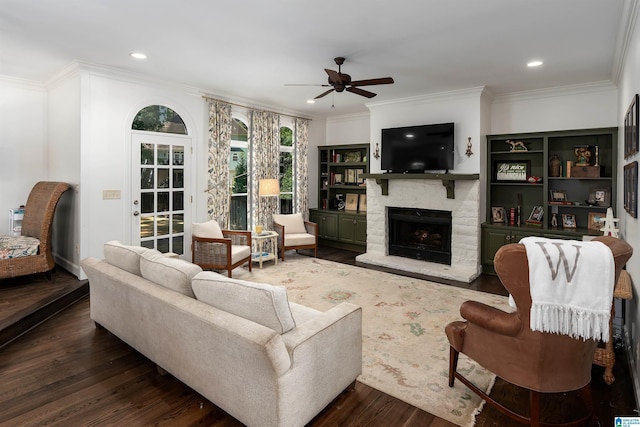 living room with ornamental molding, a stone fireplace, ceiling fan, dark wood-style floors, and recessed lighting