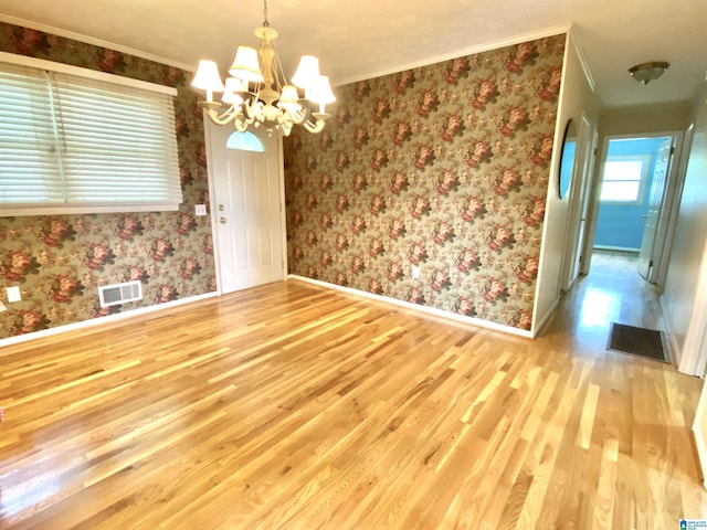 unfurnished dining area featuring crown molding, visible vents, wood finished floors, and a notable chandelier