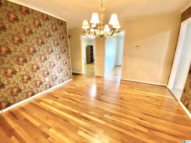 unfurnished dining area with an inviting chandelier, baseboards, ornamental molding, and light wood-type flooring