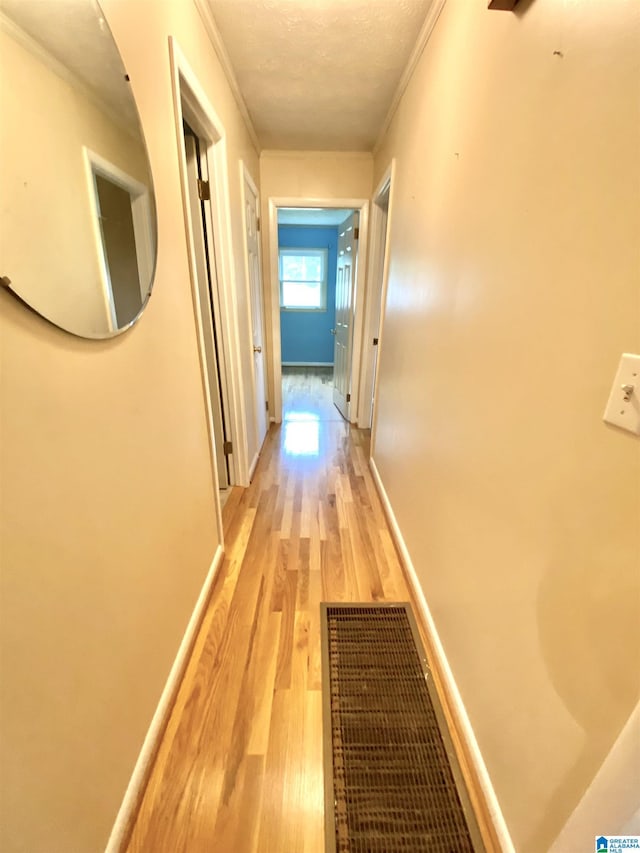 hallway featuring visible vents, light wood-style flooring, crown molding, and baseboards