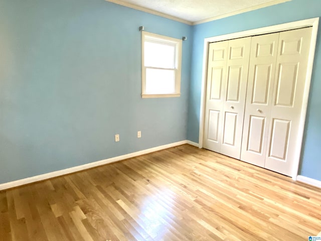 unfurnished bedroom featuring baseboards, ornamental molding, light wood-style flooring, and a closet