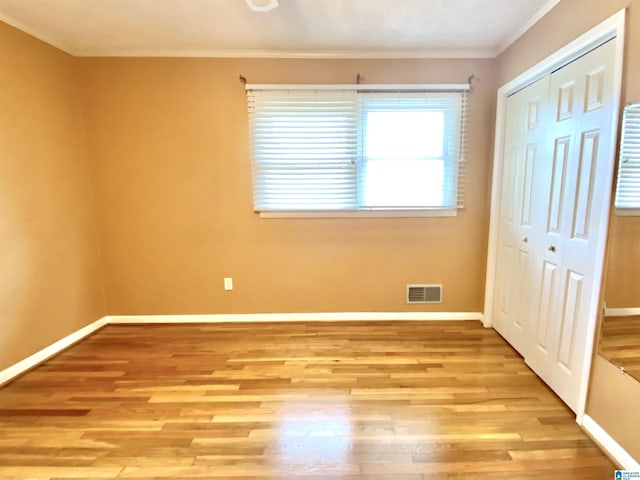 unfurnished bedroom featuring visible vents, wood finished floors, baseboards, a closet, and ornamental molding