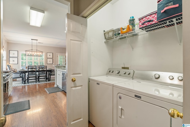 washroom with laundry area, separate washer and dryer, a chandelier, wood finished floors, and ornamental molding