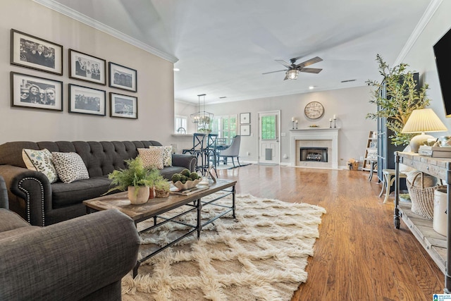 living area featuring crown molding, a fireplace, wood finished floors, ceiling fan with notable chandelier, and recessed lighting