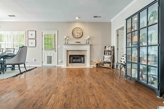 living area with crown molding, wood finished floors, a tile fireplace, and visible vents