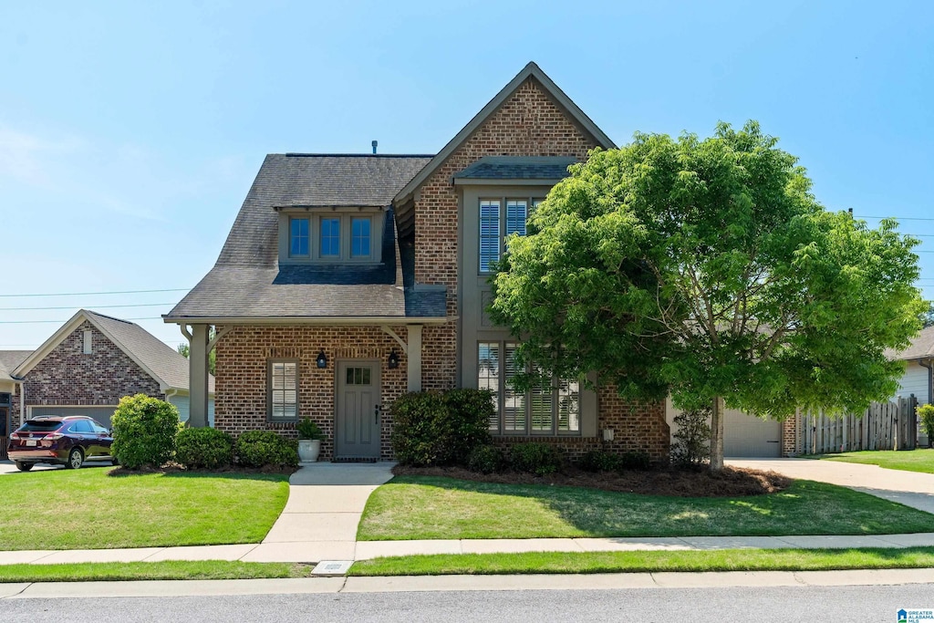 view of front of house featuring brick siding, roof with shingles, a front yard, and concrete driveway