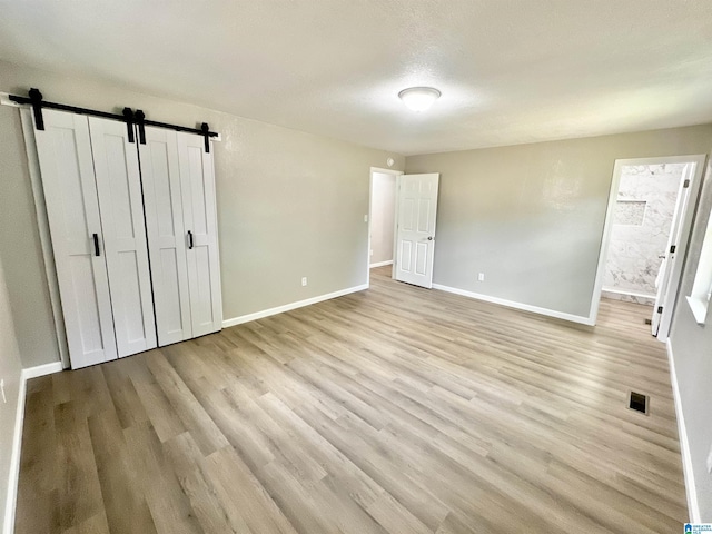 5482 Hackberry Ln N, Gadsden, AL 35903 - unfurnished bedroom featuring baseboards, light wood finished floors, a barn door, and visible vents