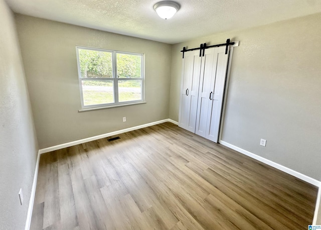 5482 Hackberry Ln N, Gadsden, AL 35903 - unfurnished bedroom featuring a barn door, a textured ceiling, baseboards, wood finished floors, and visible vents