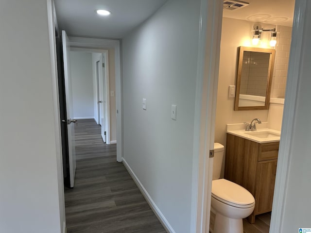 hallway featuring baseboards, visible vents, a sink, and dark wood finished floors