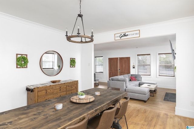 dining area with crown molding, baseboards, light wood-style floors, and a notable chandelier