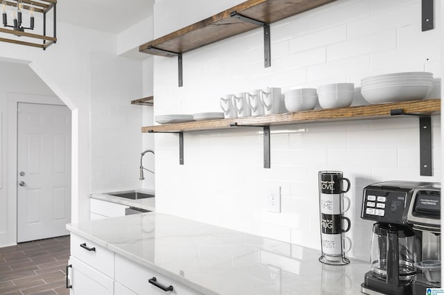 kitchen featuring open shelves, white cabinets, light stone counters, a sink, and backsplash