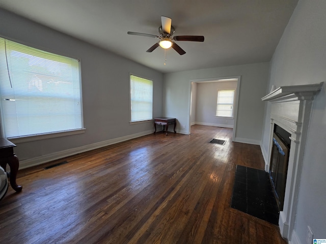 unfurnished living room with visible vents, dark wood-style flooring, baseboards, ceiling fan, and a fireplace with flush hearth
