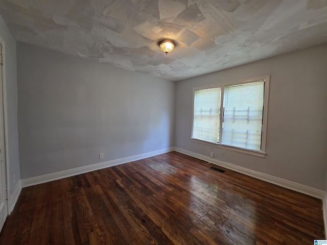 empty room featuring visible vents, dark wood finished floors, and baseboards