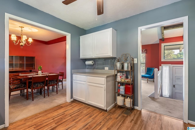 kitchen with light countertops, ceiling fan with notable chandelier, light wood-type flooring, and white cabinetry