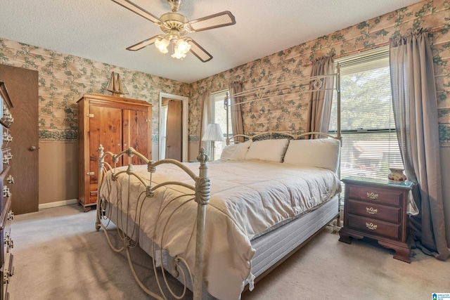 bedroom with ceiling fan, light colored carpet, a textured ceiling, wallpapered walls, and baseboards