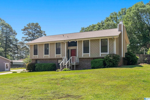 bi-level home featuring brick siding, fence, a front yard, and a chimney