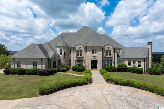french country home with brick siding, a chimney, a shingled roof, and a front yard