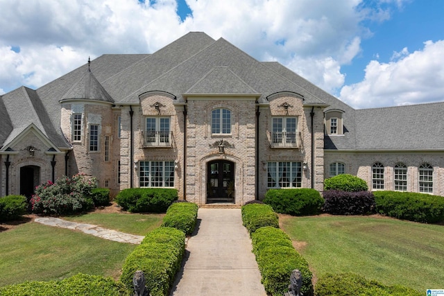 french country style house with brick siding, a front lawn, roof with shingles, and french doors