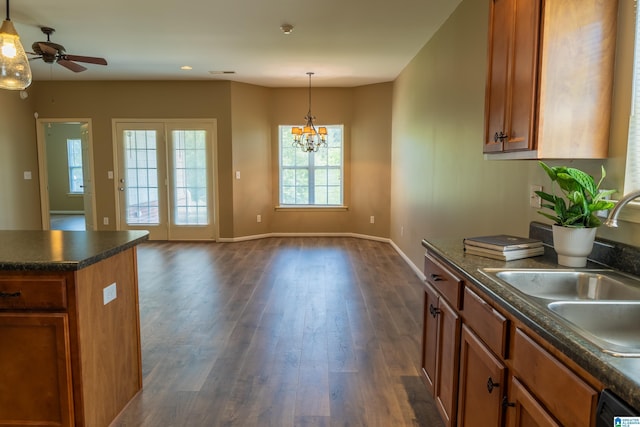 kitchen with dark countertops, a sink, dark wood finished floors, brown cabinetry, and ceiling fan with notable chandelier