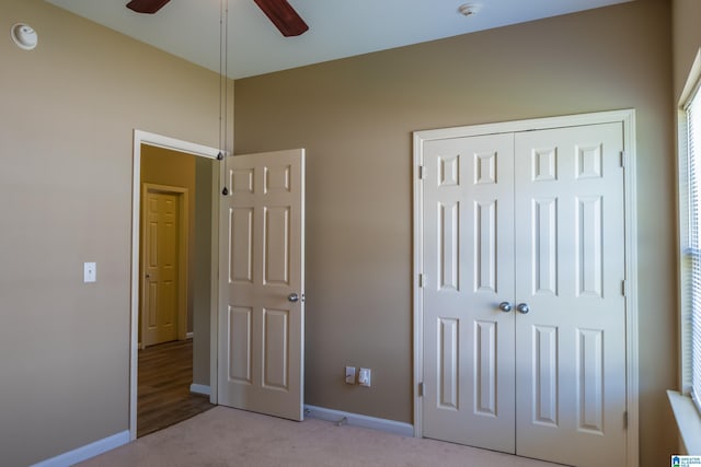 unfurnished bedroom featuring baseboards, ceiling fan, a closet, and light colored carpet