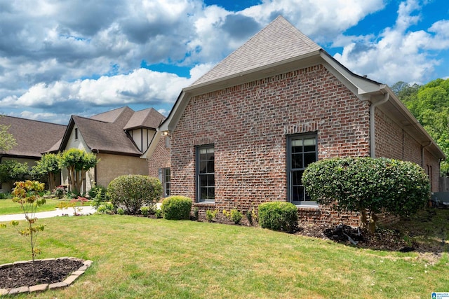 view of side of home featuring brick siding, a shingled roof, and a yard