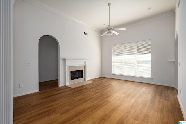 unfurnished living room with a ceiling fan, visible vents, a tiled fireplace, arched walkways, and crown molding