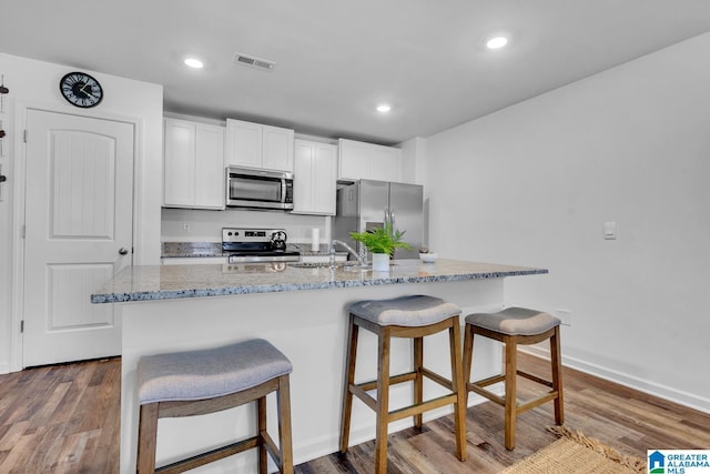 kitchen with appliances with stainless steel finishes, a breakfast bar, a sink, light stone counters, and visible vents