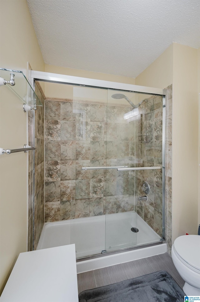 bathroom featuring a textured ceiling, toilet, and a shower stall