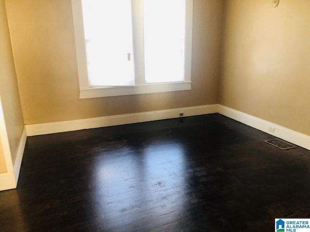 unfurnished room with baseboards, dark wood-type flooring, and visible vents