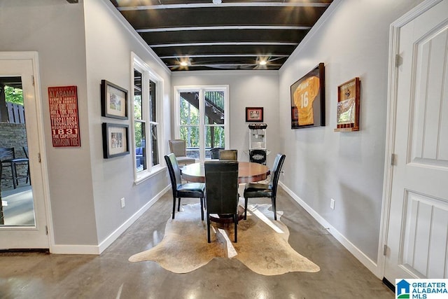 dining area with baseboards, finished concrete flooring, and beamed ceiling