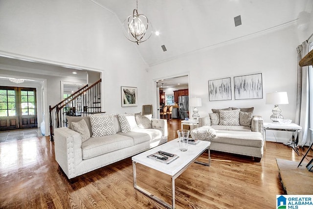 living room with crown molding, wood finished floors, high vaulted ceiling, a chandelier, and stairs