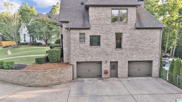 view of side of home featuring roof with shingles, a lawn, fence, concrete driveway, and an attached garage