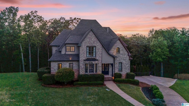 french country home with roof with shingles, a front lawn, and stone siding