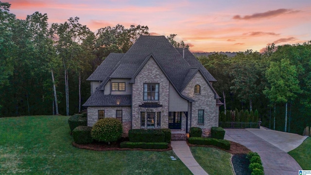 french provincial home with a shingled roof, a front lawn, and stone siding