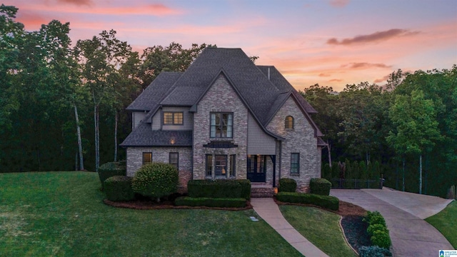 french country home featuring a lawn, a shingled roof, and stone siding